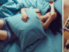 Frau liegt im Bett mit Kissen auf dem Bauch und Arm über dem Gesicht