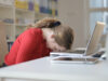 Weiblich gelesene Person am Schreibtisch legt den Kopf auf den aufgeklappten Laptop